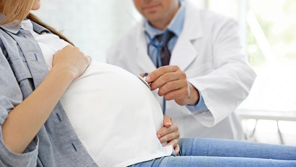 Le gynécologue en blouse vérifie le ventre d'une patiente enceinte avec un stéthoscope dans son cabinet.