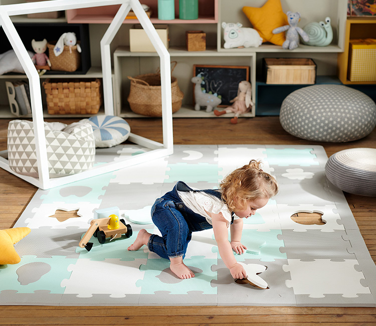Une petite fille d'un an et demi joue dans sa chambre d'enfant sur le tapis en mousse LUNO Shapes de Kinderkraft, en faisant des puzzles.