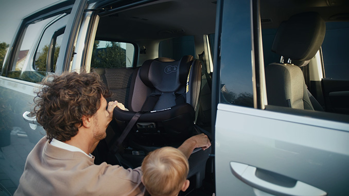 Un père fait pivoter un siège auto dans sa direction, prêt à installer son enfant, qui se trouve à côté de lui.