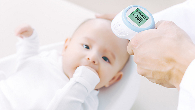 Un nouveau-né est allongé chez un médecin et tient sa main dans sa bouche. Le médecin mesure sa température avec un thermomètre sans contact - elle est de 36,6°C. 