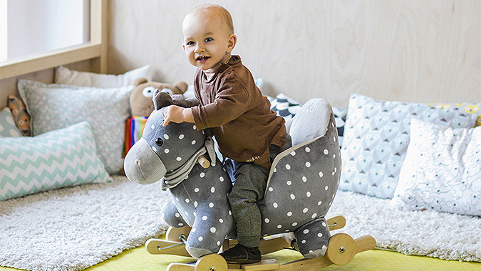 Dans une chambre d'enfant, un petit bébé assis sur un cheval à bascule.