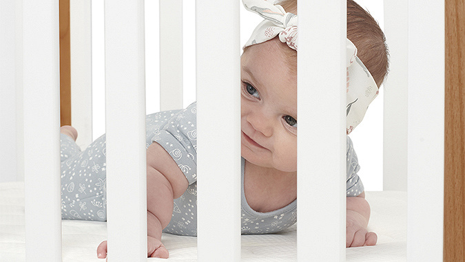 Un nouveau-né sur un matelas confortable regarde à travers les barreaux du lit de la marque Kinderkraft.